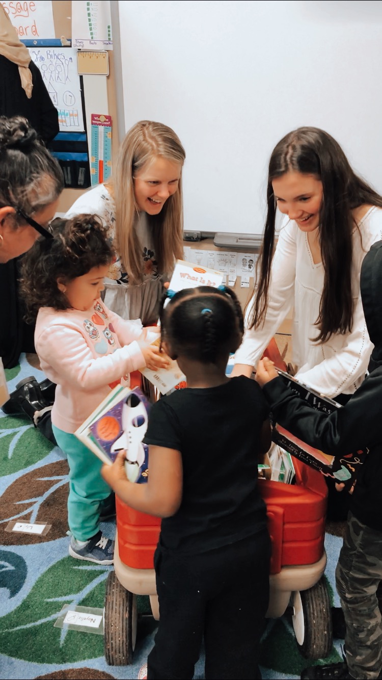 Two girls spend time with smiling school children.