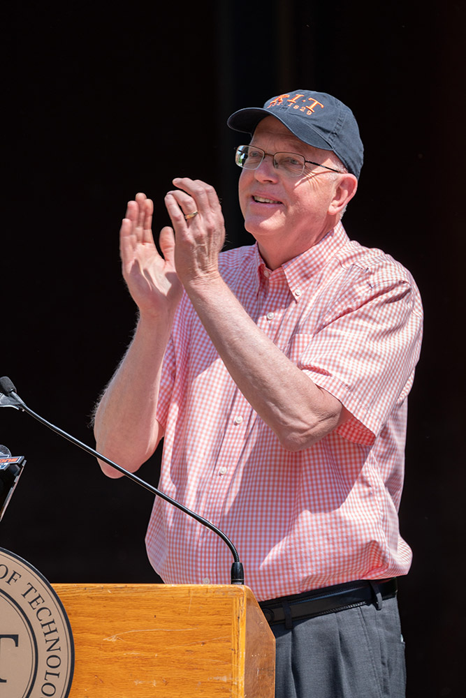 man clapping at podium outdoors.