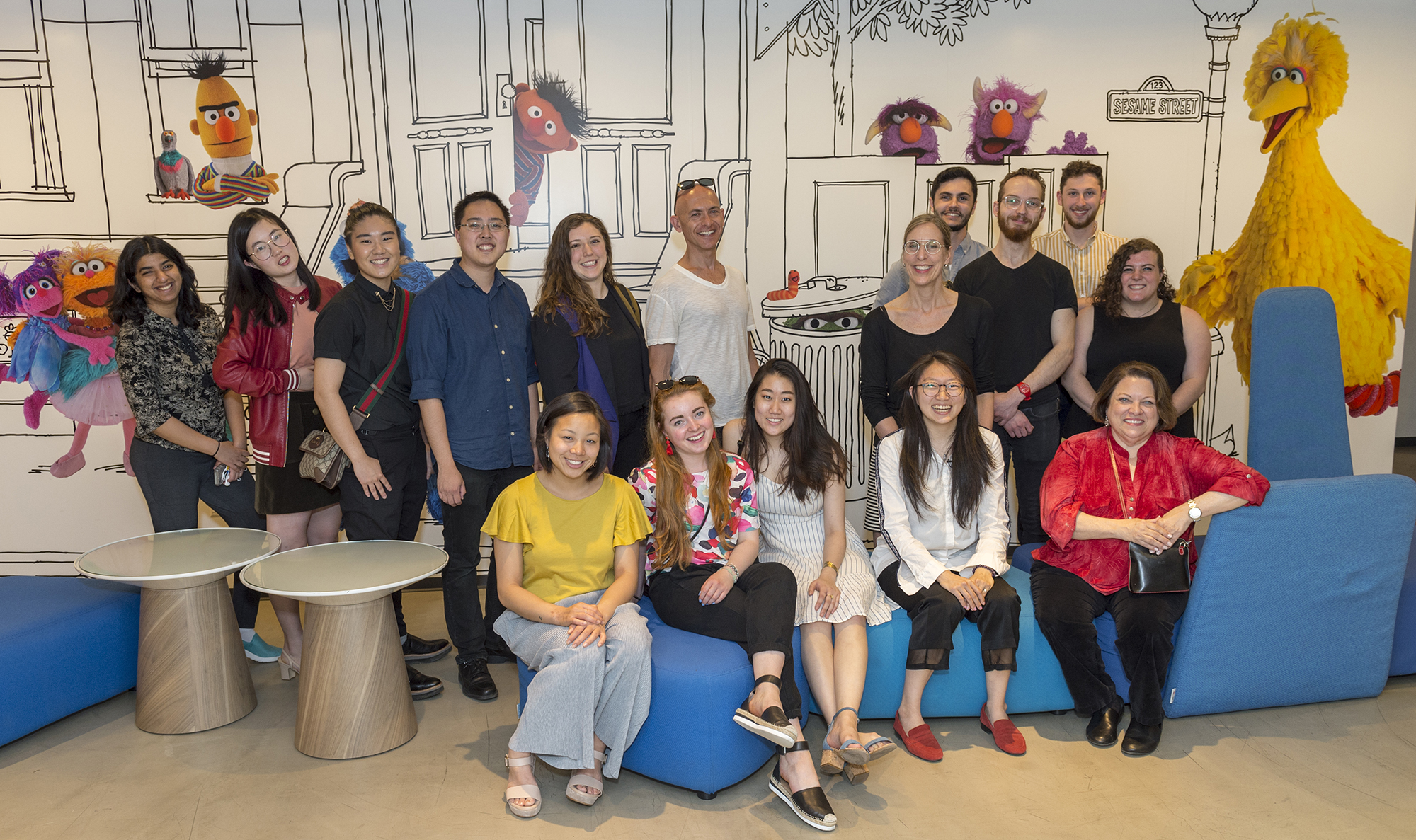 A group picture of faculty and students with Sesame Street puppets on the wall.