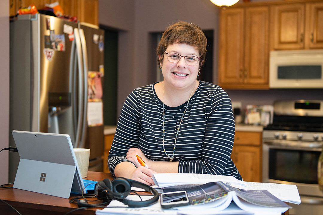 Woman stands at kitchen island with papers and tablet computer.