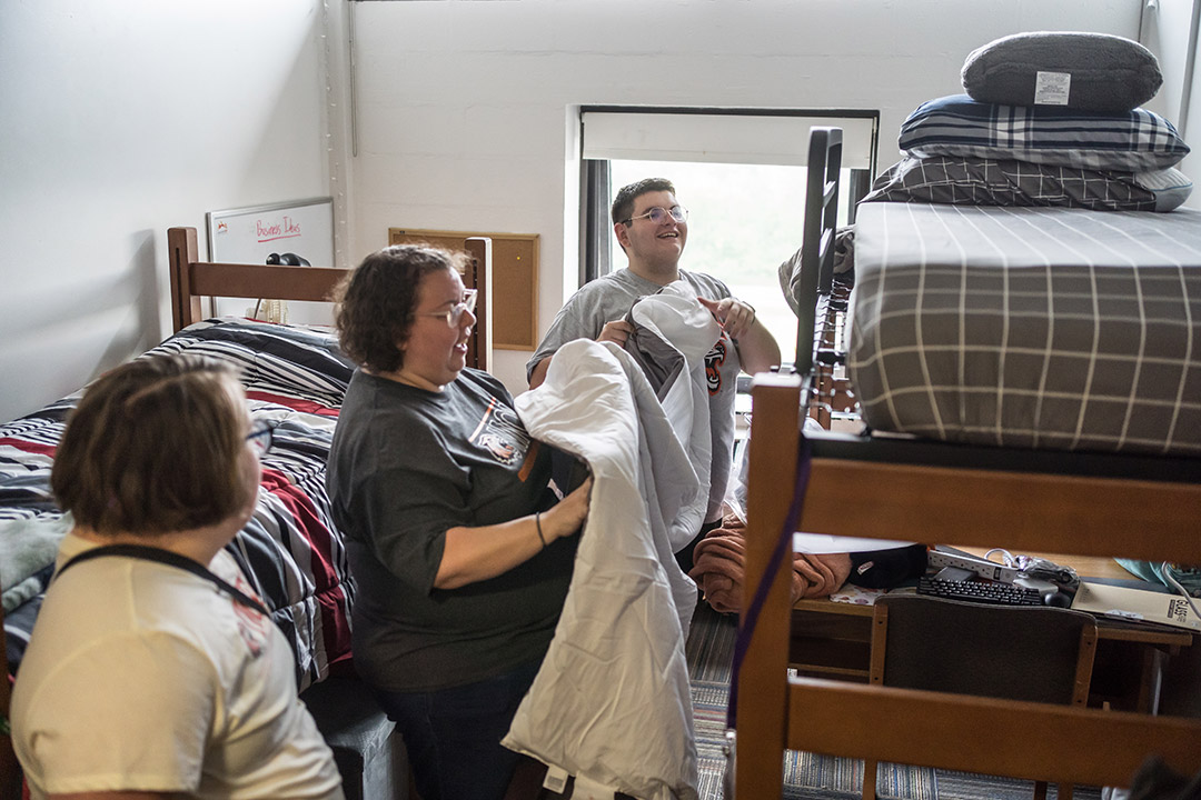 a mother, sister and college student standing in a dorm room in front of a bunk bed.