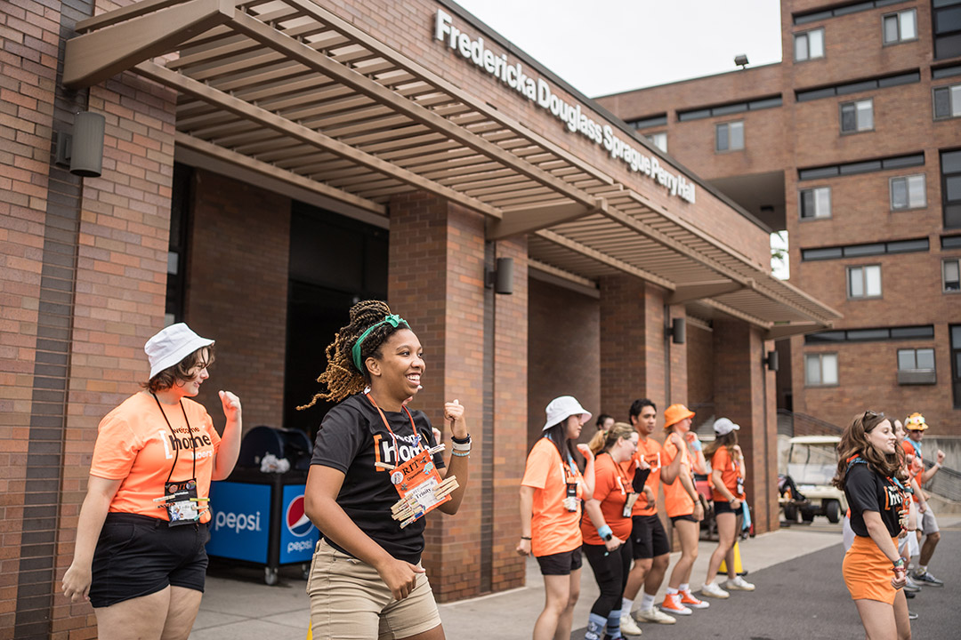 line of orientation leaders dancing outside of a residence hall.
