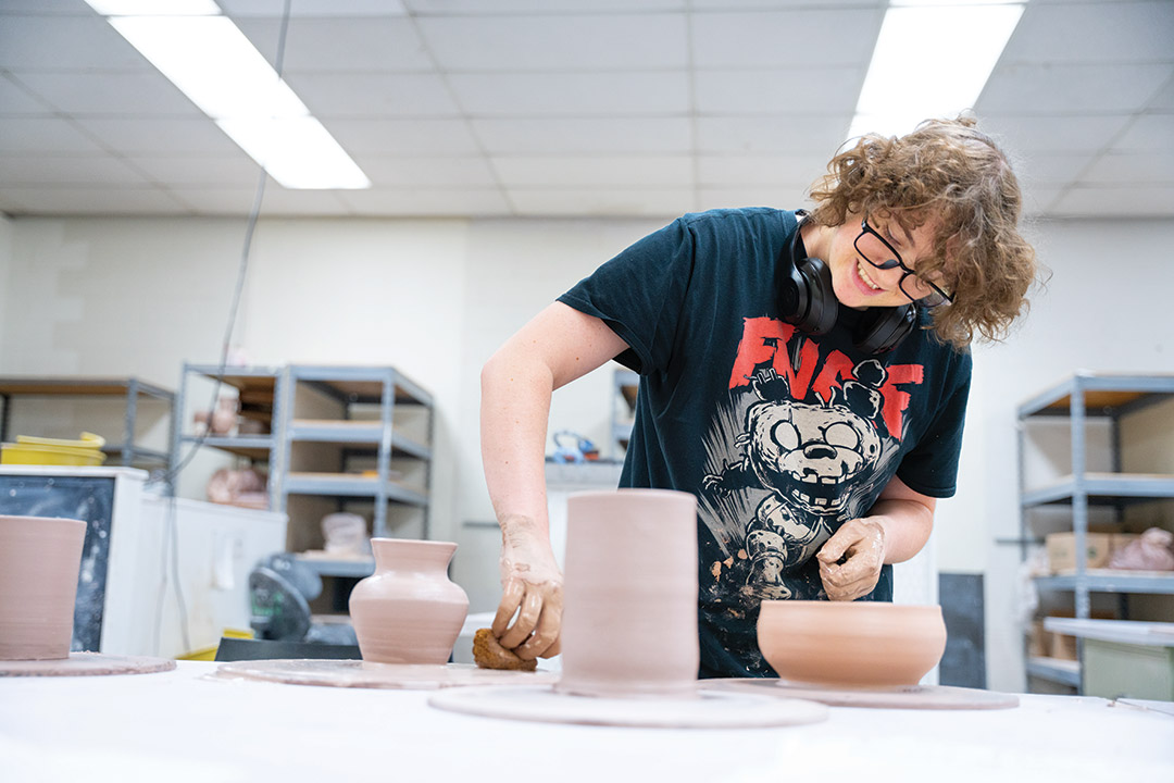 college student using a wet sponge around the base of a pottery piece.