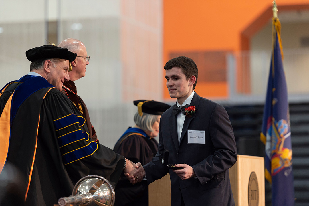 Student shakes hands with staff member dressed in regalia.