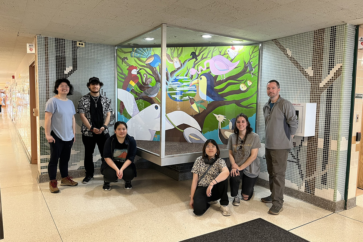Students and faculty stand in front of a mural.