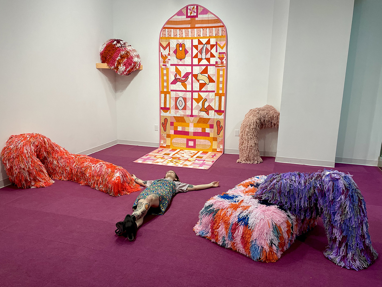 Shayna Kiblin lays next to sculptural pieces in their thesis exhibition at City Art Space.