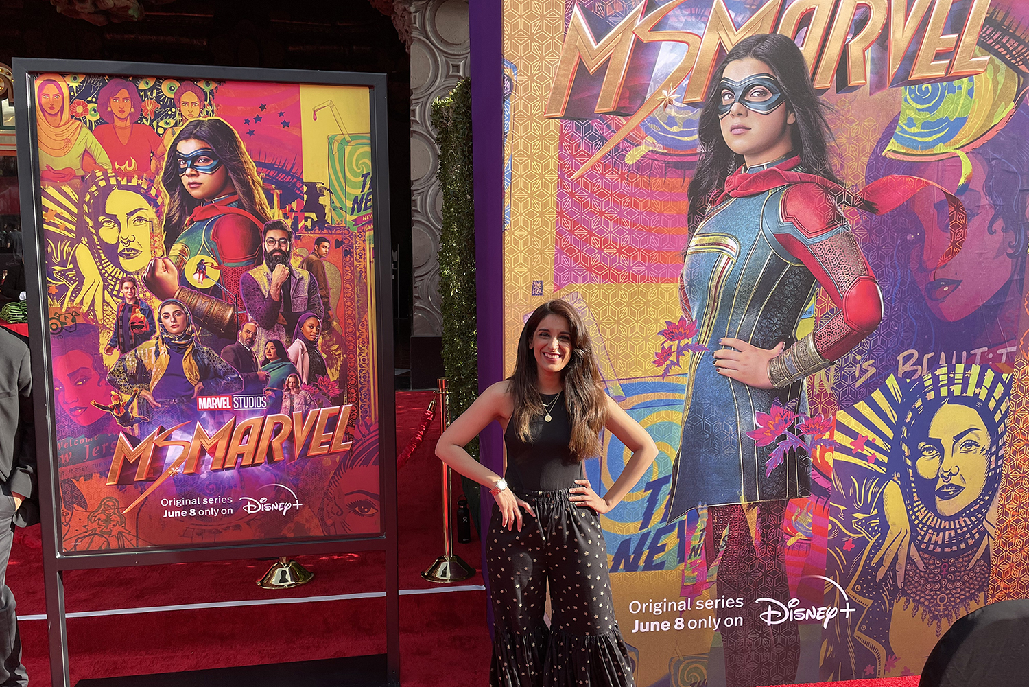 Shehzil Malik stands in front of a Ms. Marvel poster that features a collage of her work.