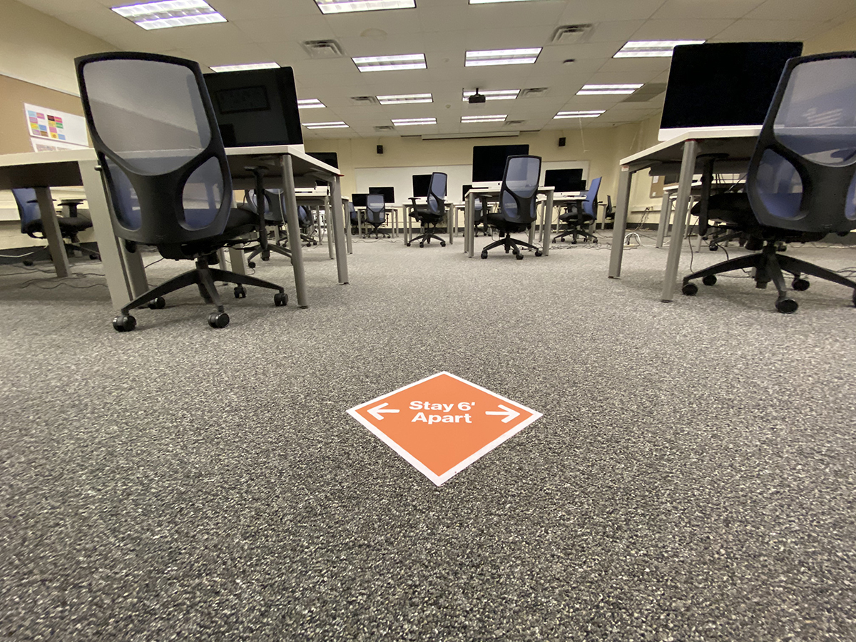 A computer lab with a sign encouraging six feet of distance.