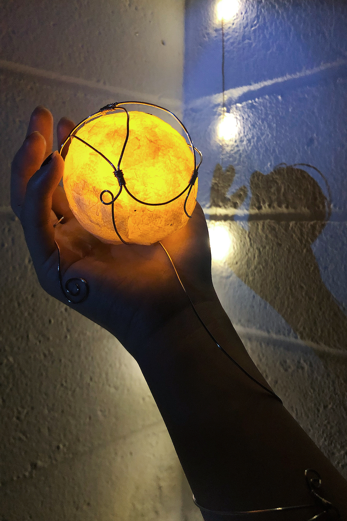 An arm holds a wired object that is lit up in a ball.