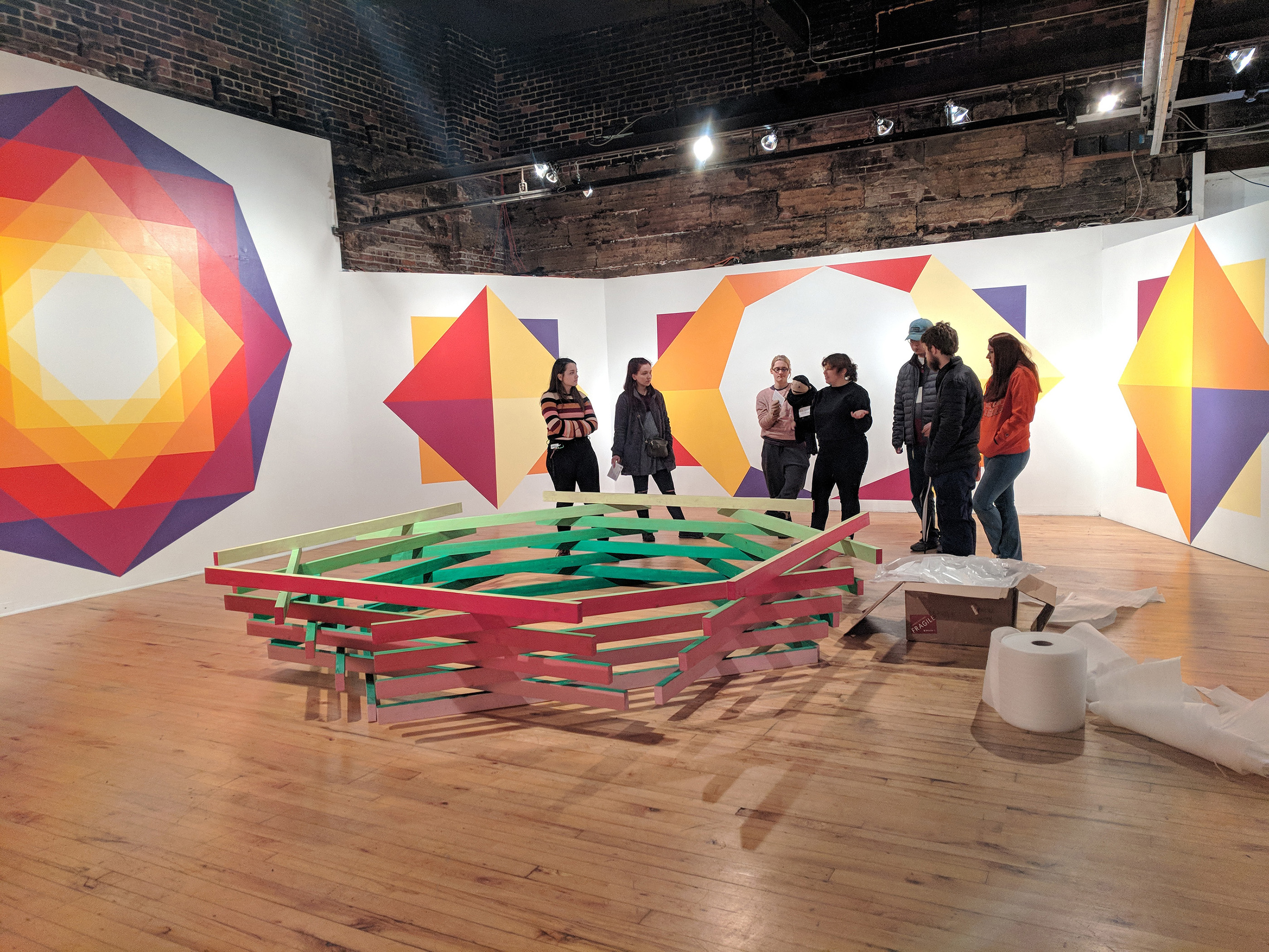 Students gather in a space with vibrant decals on the walls and an installation in the center of the room.