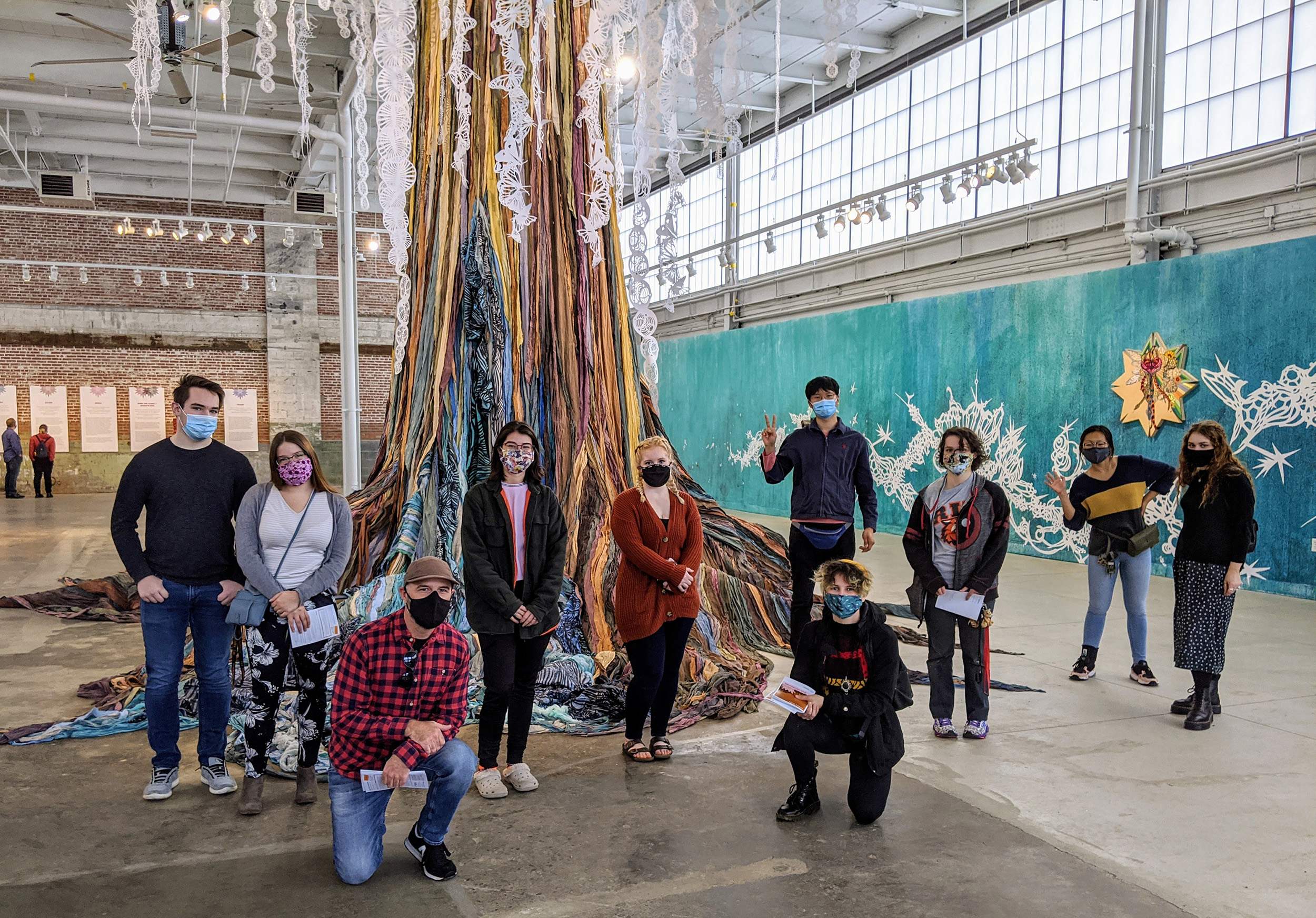 A group of students gather around a large sculpture that resembles a tree.