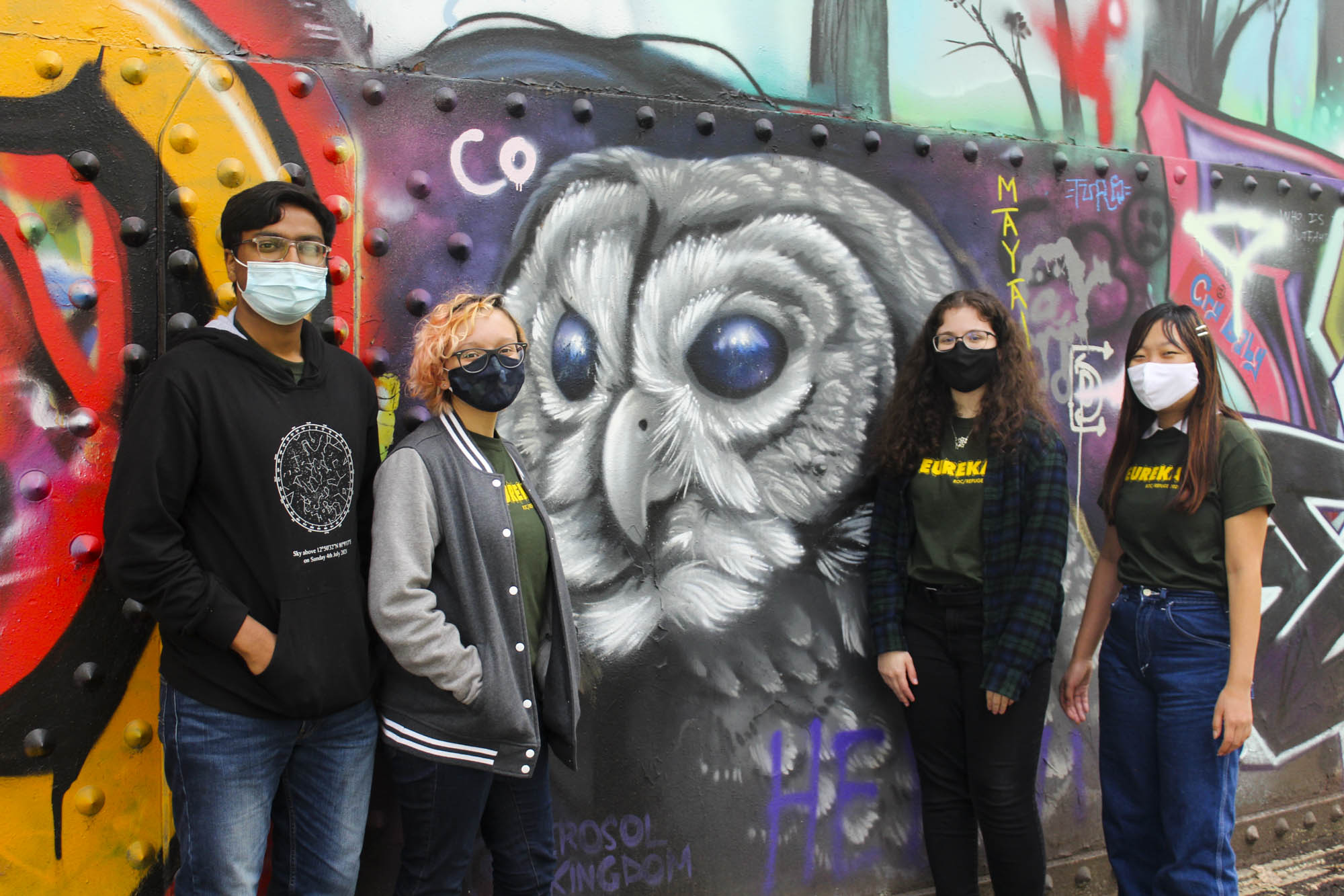 A group of students pose in front of a mural.