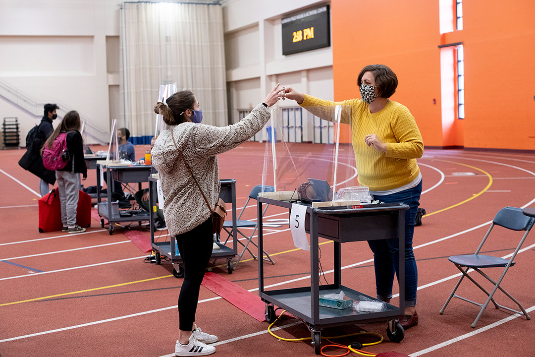 volunteer handing COVID test vial to student across a clear barrier.