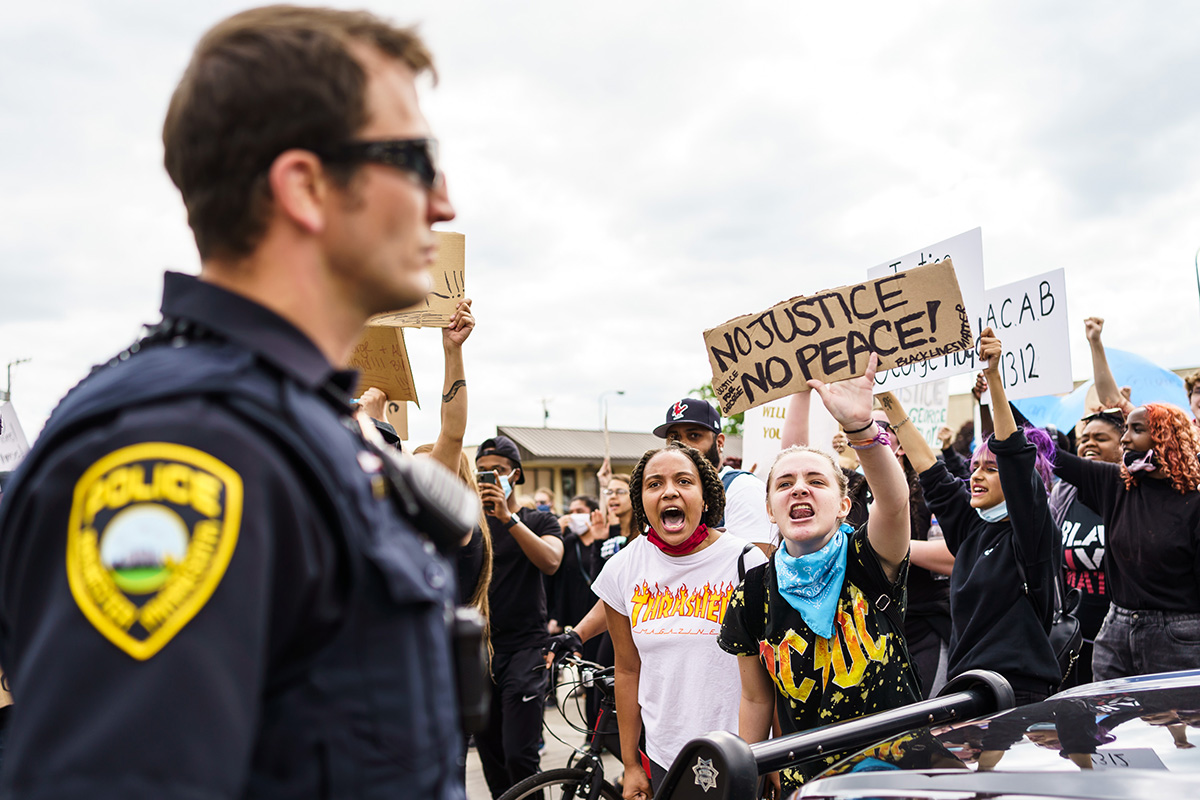 A crowd of protesters hold up signs as a police officer looks on.