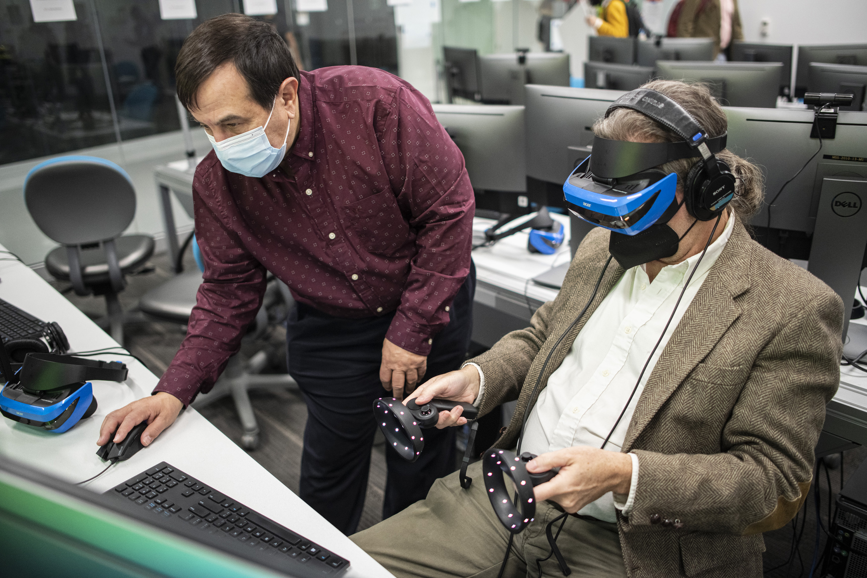 Faculty Joe Geigel toggles a computer mouse while someone else wears a VR headset.