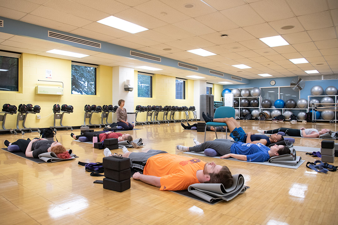 Students lay on gym floor in yoga poses.