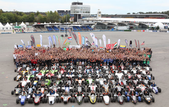 People and formula cars gathered on a race track.