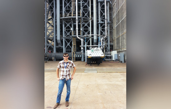 Grow standing in front of space launch system in a flannel shirt and sunglasses.