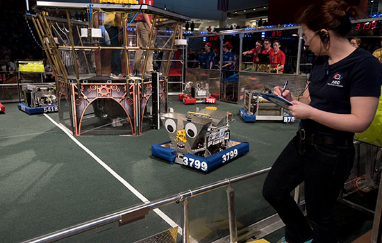 A person writing on a clipboard while looking at a robot.