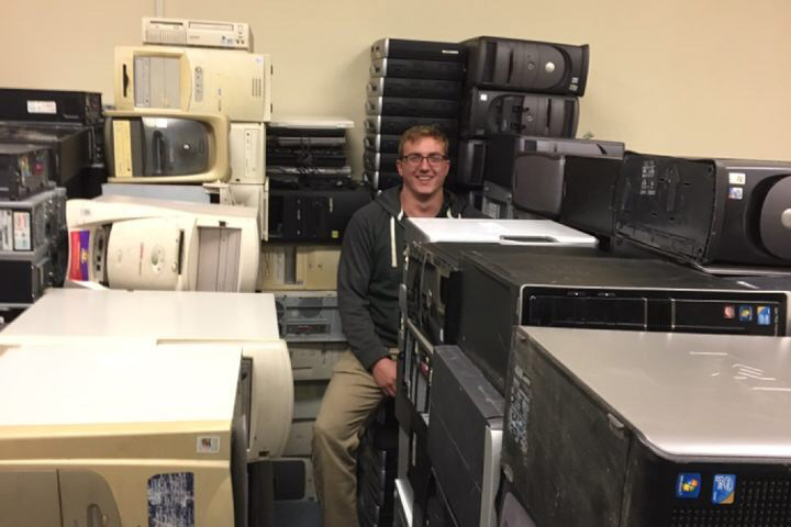 Josh Geise sits among stacks of computers, his head poking out from the top of a stack.