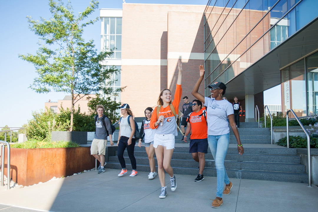 A group of students walking together on campus, two girls giving each other a high five.