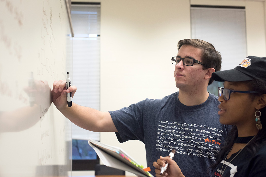 Students standing in front of a white board while they work with different formulas.