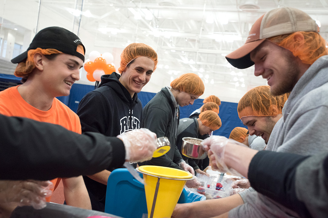 Students in orange hairnets working together to prepare a meal.