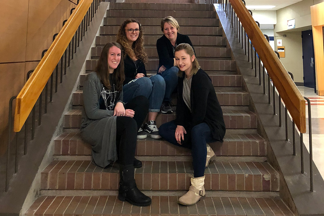 The four students who collaborated on the art space design pose for a photo on a brick staircase.