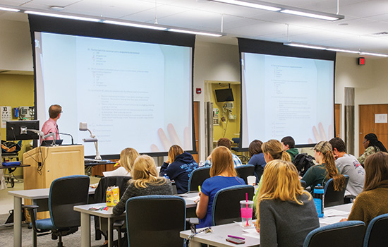 Classroom of students looking at two screens with projections.