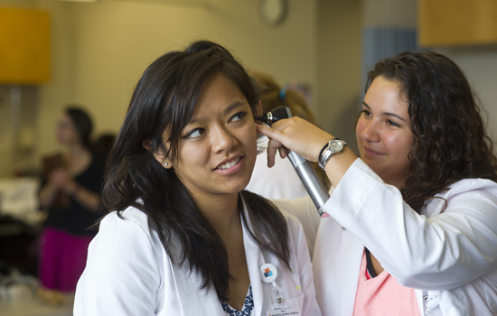 Alexandra Williams examines her partner's ear with an otoscope.