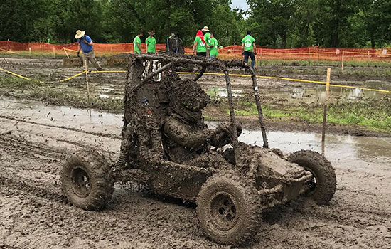 Baja driver in car covered in mud on track.