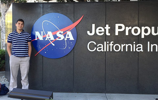 Erez Binyamin poses for a photo next to a large NASA sign outside of the Jet Propulsion Center.