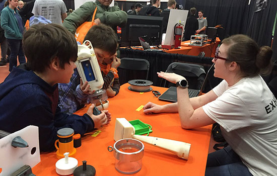 Cayla Denning sits at a table and demonstrates the prototype device for three young boys.