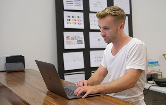 A photo of Cole Johnson standing at a high-top desk and working on his laptop.