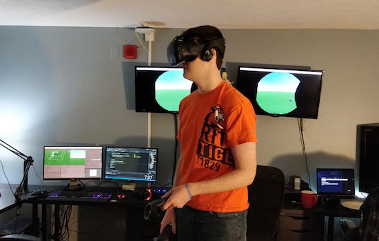 Student wearing a virtual reality headset standing in front of computer monitors.
