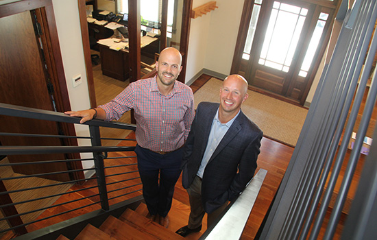 Justin Hamilton and Christopher Stern pose for a photo on a set of modern-looking stairs.