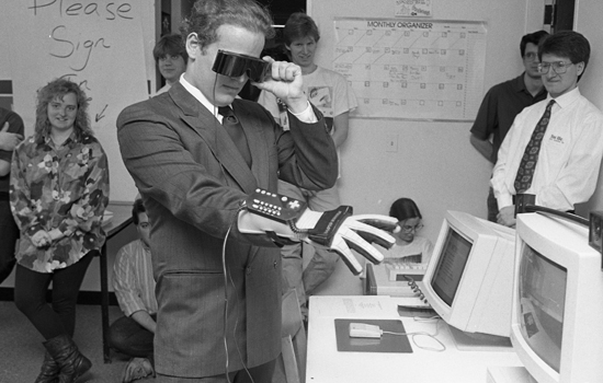 black and white photo of person using goggles and a glove with a computer controller on it.
