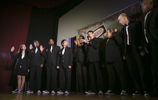 group of college students all wearing black suits and converse sneakers standing in a line on a stage.