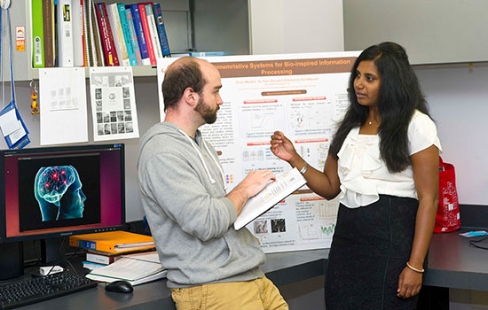 Dhireesha Kudithipudi converses with a student in her office, a research poster hanging behind them.