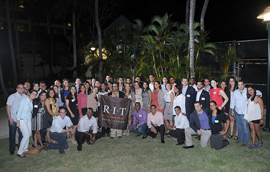 large group of people posing outside at night with an R I T banner.