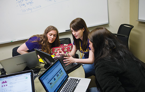 three students collaborate while looking at laptop screen.