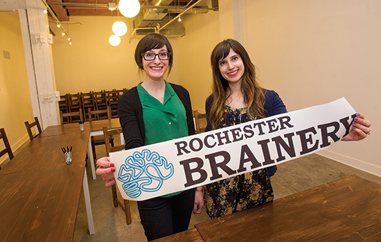 Two people holding "Rochester Brainery" poster