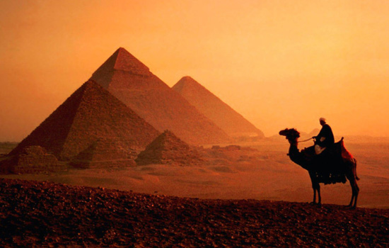 Person riding camel with pyramids in the background