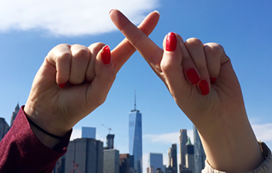 Hands making a cross with the New York City Skyline