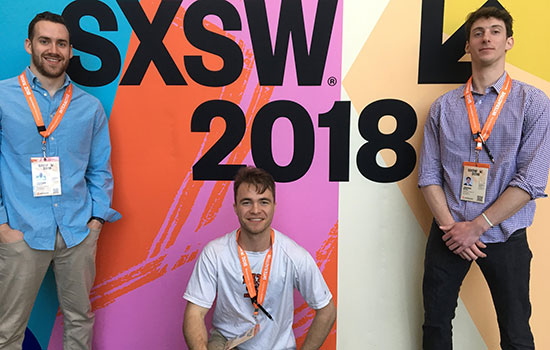 Three team members standing in front of a colorful wall that says "SXSW 2018".