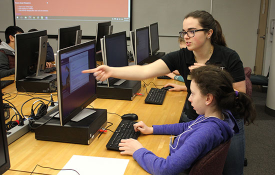 RIT student pointing to computer screen teaching grade school student.