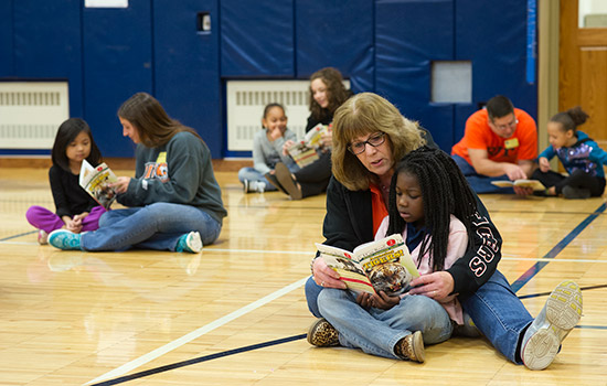 Adults reading to kids in a gym.