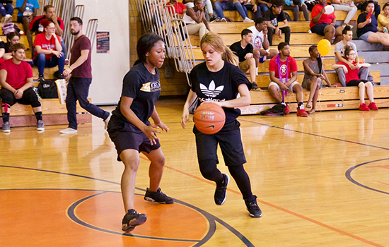 Two people playing basketball with people in the bleachers.