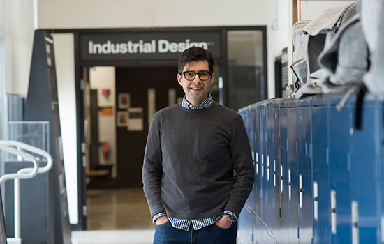 Alex Lobos standing next to lockers under a sign that says "Industrial Design".