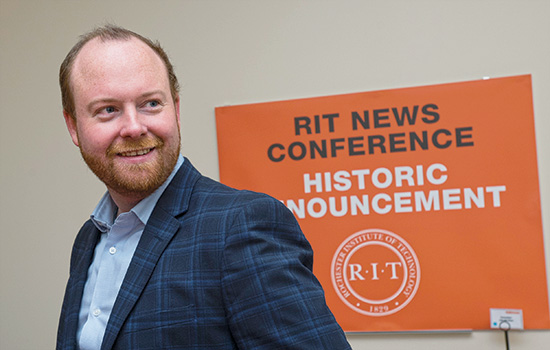 man standing in front of sign that reads: RIT News conference: historic announcement.